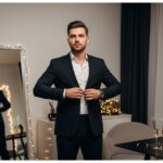 Muž si upravuje černé sako před zrcadlem v moderním bytě na Silvestra s dekoracemi a sklenicemi šampaňského